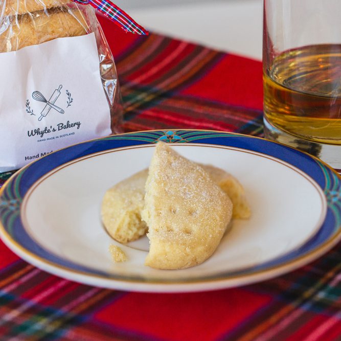 Highlanders Traditional shortbread Two shortbread cookies on a plate, with a glass of whisky and a Scottish tartan tablecloth.