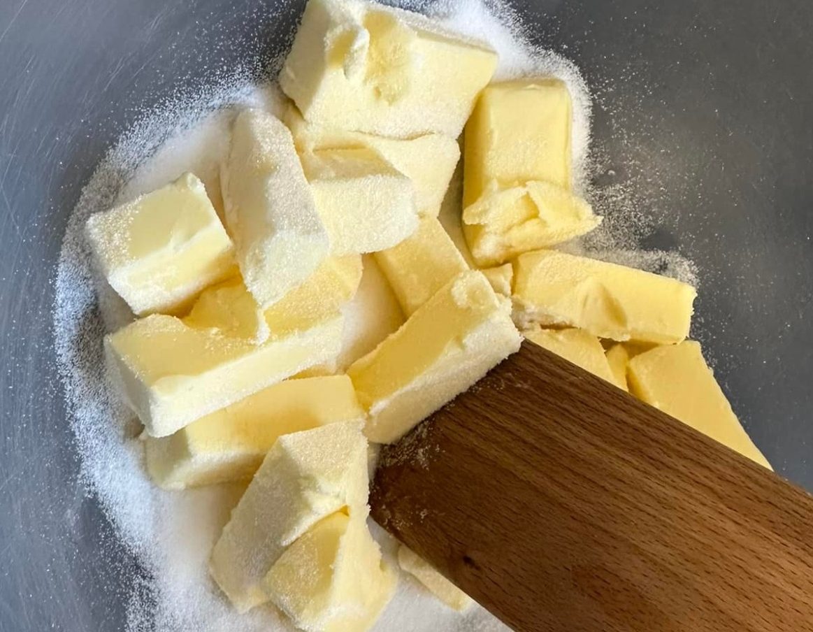 Whyte's bakery shortbread ingredients Chunks of butter on a bed of sugar with a wooden spoon for mixing.